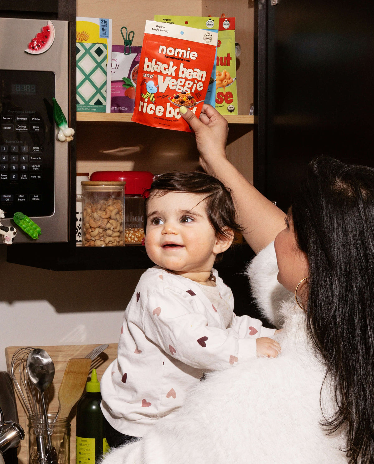 Woman holding a child in a kitchen with books on a shelf in the background